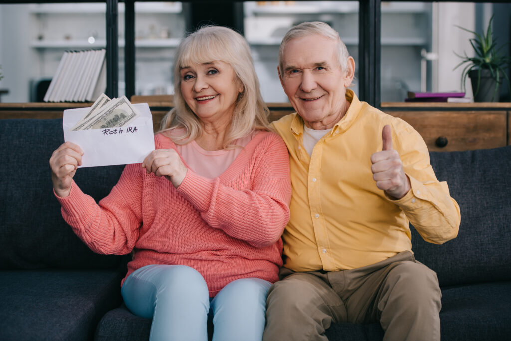 senior couple showing thumb up sign while holding envelope with 'roth ira' lettering and dollar